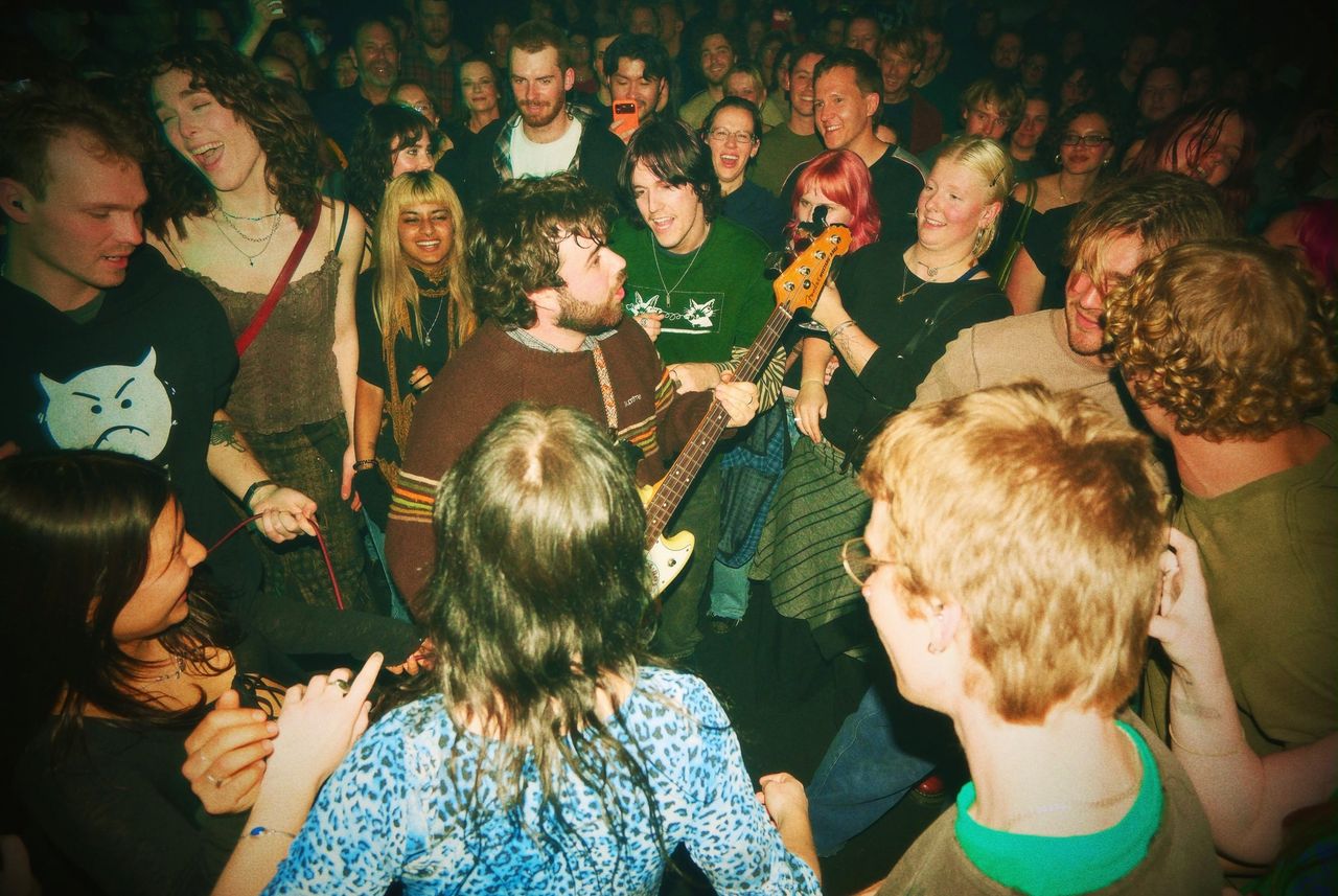 Band member of Swapmeet playing bass guitar in the middle of an energetic, cheering crowd during a live gig.